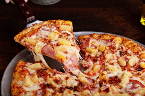 Hawaiian pizza with one slice being pulled apart