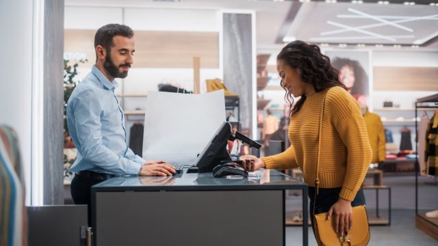 Young Woman at Counter Buys Clothes from Friendly Retail Sales Assistant,