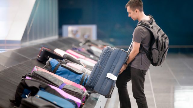 A young man grabbing his checked luggage from a carousel