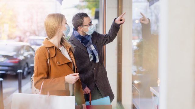 Couple doing shopping during partial lockdown standing in front of shop window with mask