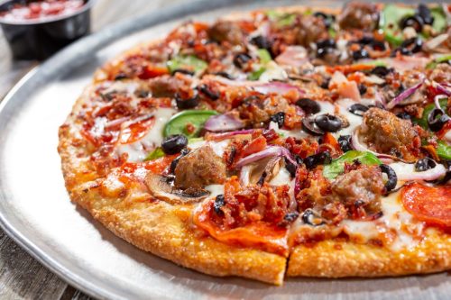 A pizza topped with meat and vegetables on a metal pan
