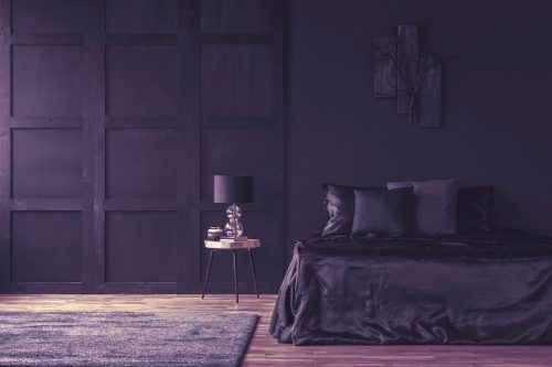Lamp on wooden table in spacious violet bedroom with matching dark-purple bedding