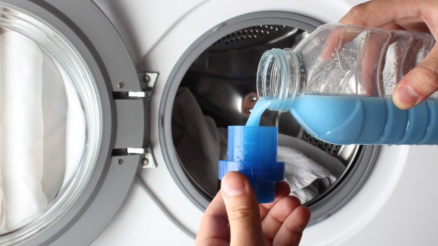 Close up of someone pouring blue fabric softener in the washing machine