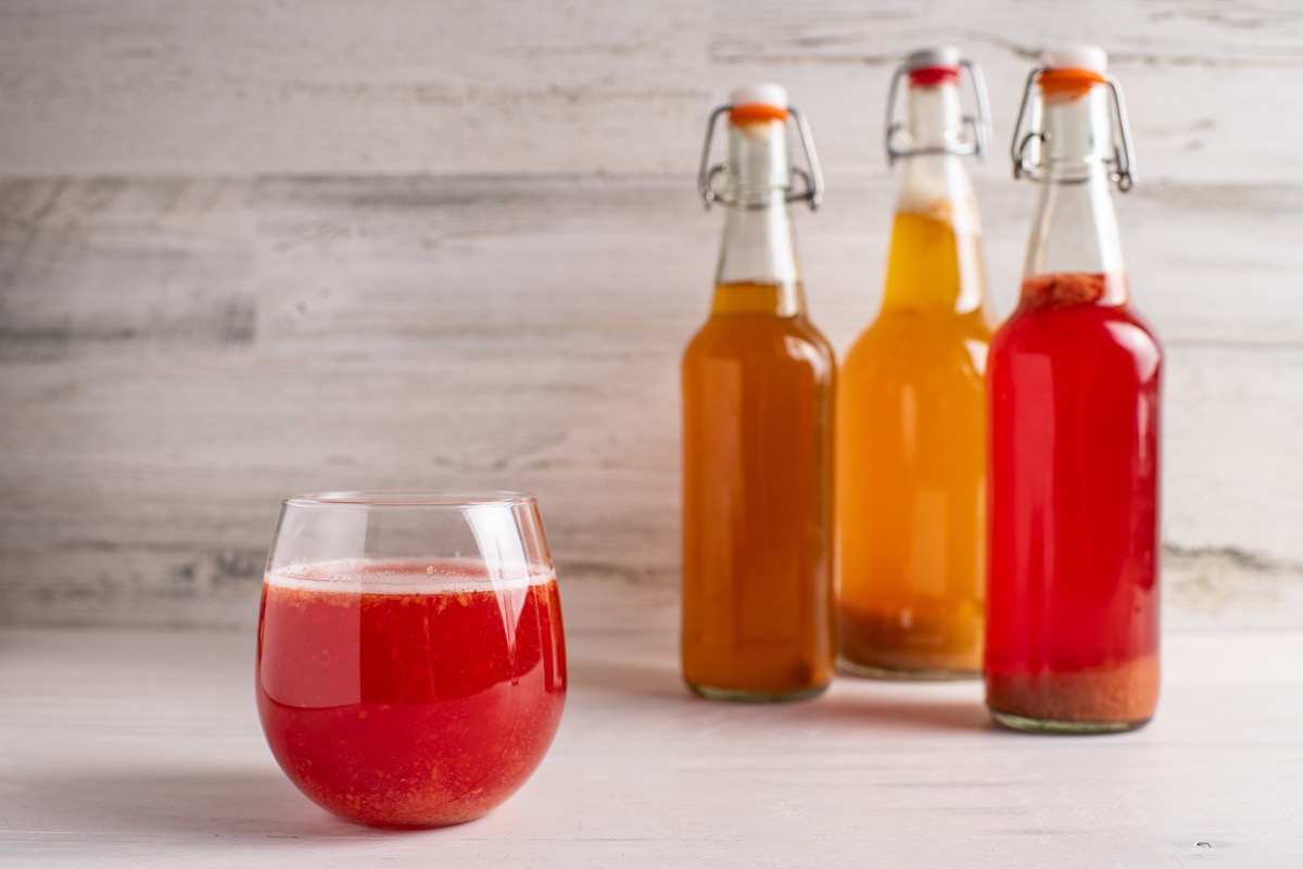 Fermented strawberry kombucha tea with plain, pineapple and strawberry bottles in the background.