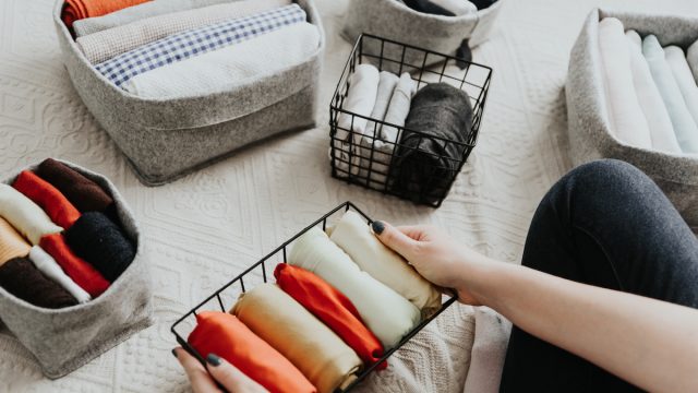 Close up of a woman organizing clothes into bins on her bed.