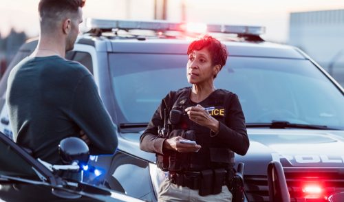 A policewoman taking a statement from a civilian outside her patrol car.