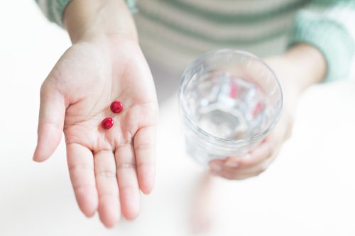 woman's hands holding two iron tablets and a glass of water