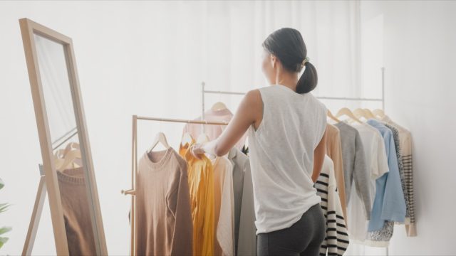 woman choosing clothes on clothes rack dressing looking herself in mirror in living room at home.