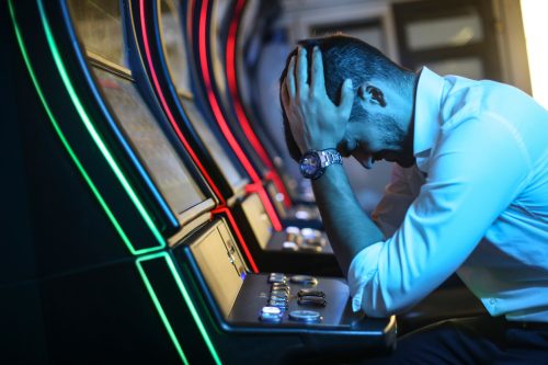 A young man sitting at a slot machine with his head in his hands