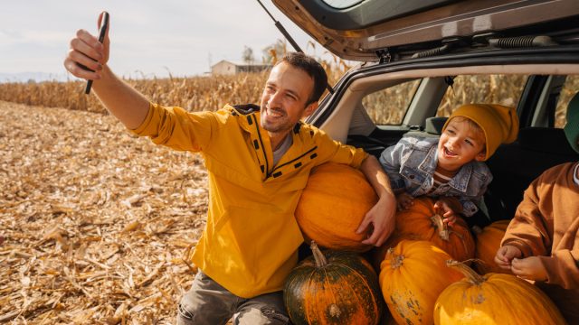Photo of a young father and his sons taking pictures in a car trunk full of pumpkins