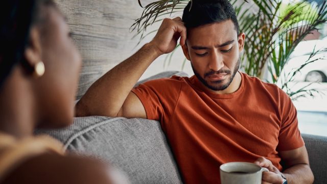 Shot of a handsome young man sitting with his girlfriend in the living room at home and looking upset