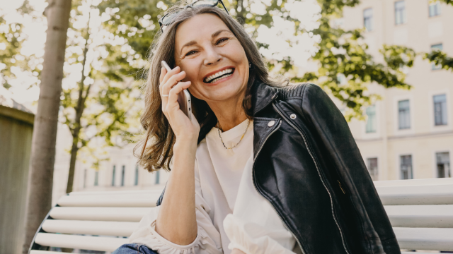 older woman leather jacket on bench on cell phone