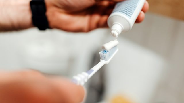 A closeup of hands squeezing toothpaste onto a toothbrush