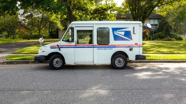 A US postal service delivery van is seen parked on a street in front of a neighborhood house