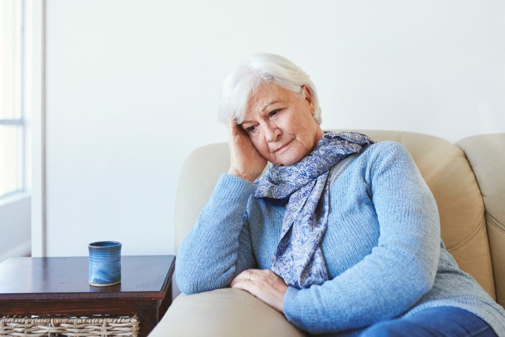 A senior woman sitting on the couch with a confused look on her face