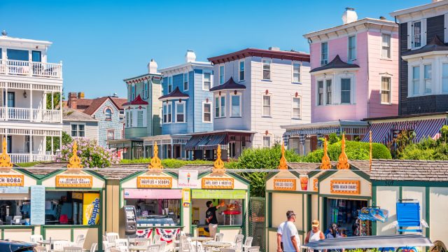 People browse vendor booths in downtown Cape May, New Jersey on a sunny summer day with colorful Victorian homes in the background.