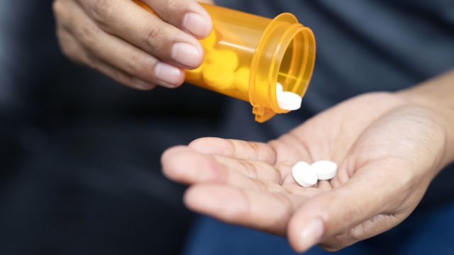 A close up of hands holding a prescription bottle and medication