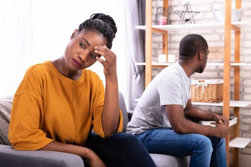 A young couple facing away from each other on the couch, with the woman looking distressed.