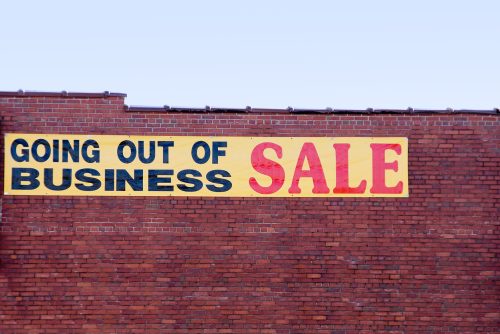 A "going out of business" sale sign hanging on the side of a brick building