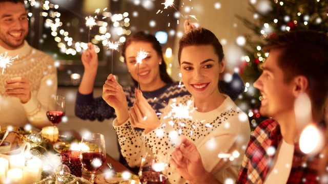 A group of happy friends at a dinner table celebrating the holidays with sparklers.