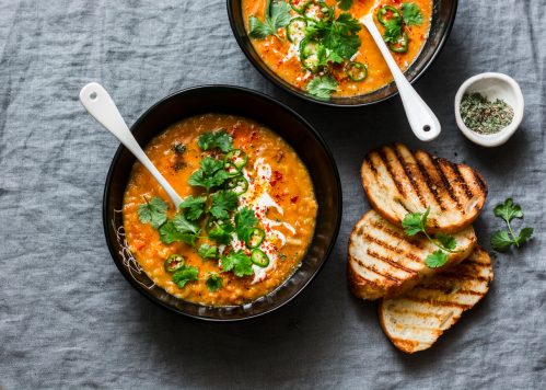Curried red lentil tomato and coconut soup - delicious vegetarian food on grey background, top view. Flat lay served healthy lunch
