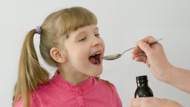 Smiling girl taking medication from a spoon.