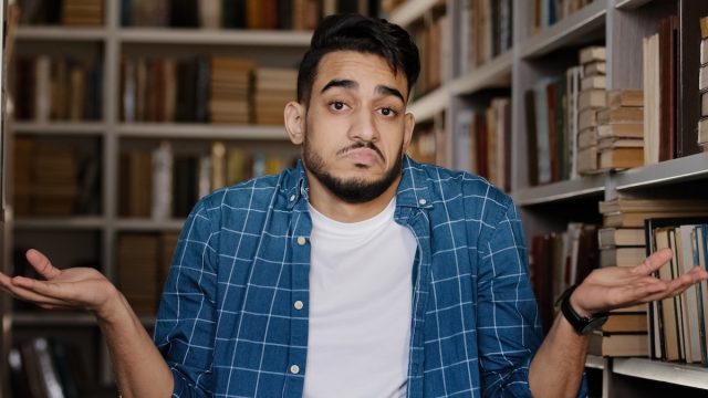A misunderstood, confused-looking man shrugging his shoulders in a library.