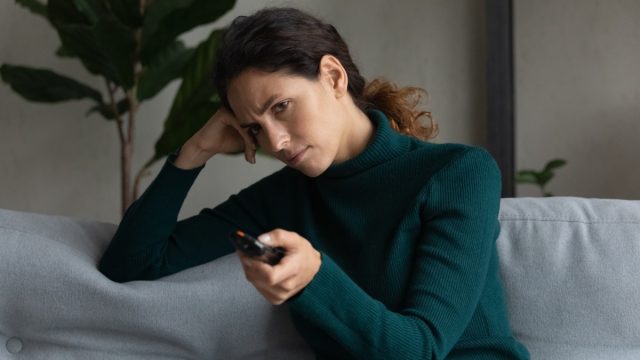 woman sit rest on sofa at home feel bored watching TV.