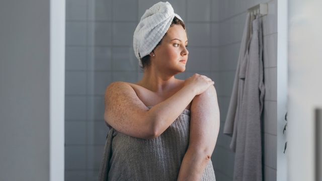 woman applying body lotion after a shower in the morning