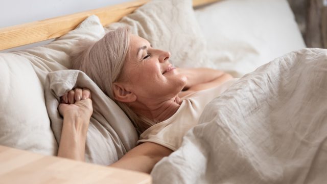 Satisfied middle-aged woman lying in bed enjoy early morning
