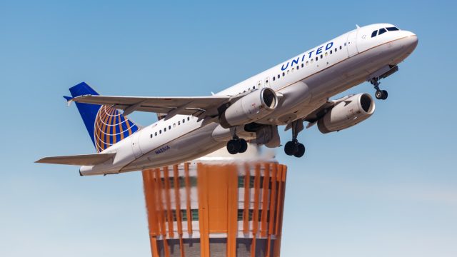 A United Airlines flight taking off from the airport with an air traffic control tower in the background