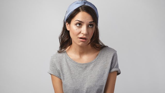 Funny emotional young Caucasian woman wearing gray top and headscarf grimacing, rolling her eyes, expressing annoyance