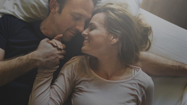 A couple sweetly holding hands in bed.