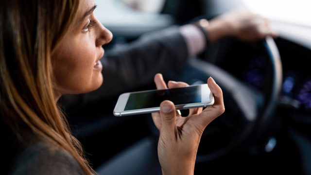 Close-up of woman using mobile phone and talking on the speaker while driving car.