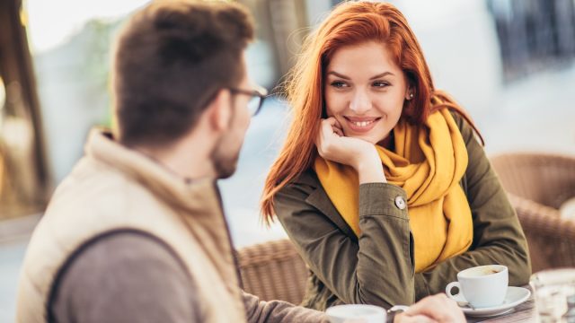 A couple sitting at an outdoor cafe; the woman is smiling and staring at her partner.