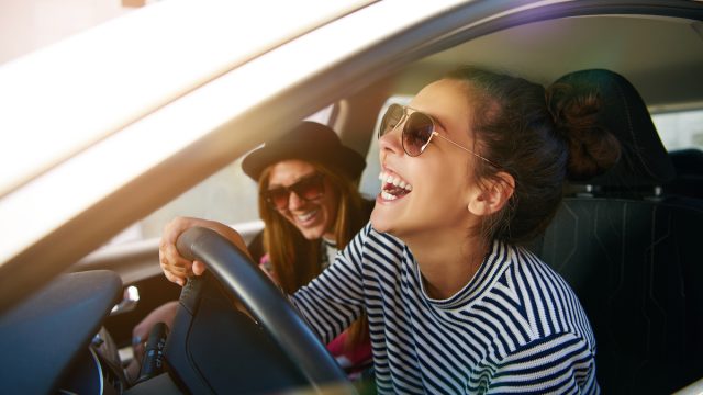 Laughing young woman wearing sunglasses driving a car with her girl friend