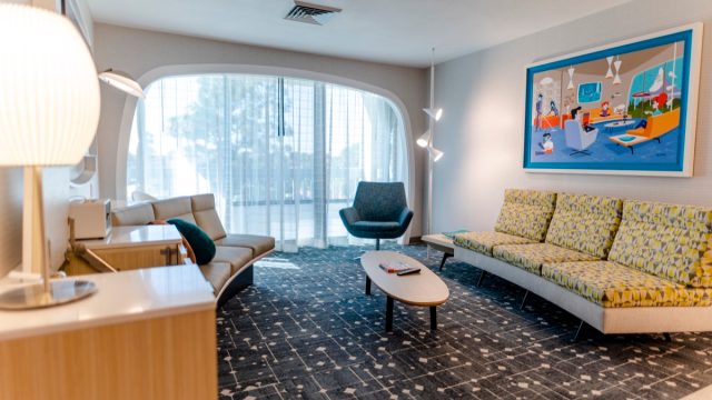 A retro-themed hotel suite with mid century modern couch, able, chair, and painting