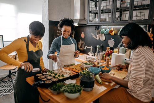 three black woman laughing and preparing dinner together