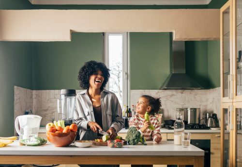 A happy mother having fun with her cute daughter while cutting vegetables.