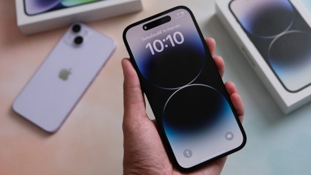 A close up of a hand holding a new iPhone 14 with its box behind it