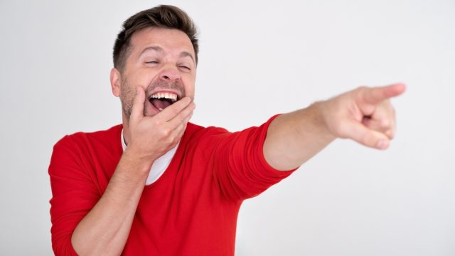 Man in a red sweater laughing and pointing at something.