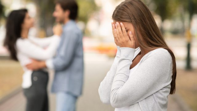 Upset woman crying, seeing her boyfriend with other girl in park