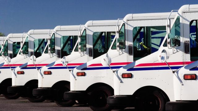 A row of US Postal service trucks, parked waiting to deliver the mail.