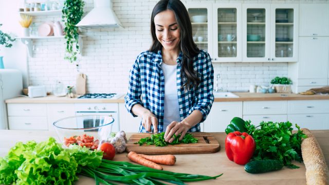 A young woman chopping vegetables on her kitchen island.