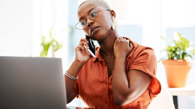 A young woman talking on the phone with a concerned look on her face while sitting in front of a laptop