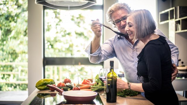 A senior couple standing in the kitchen and trying a taste over the stove