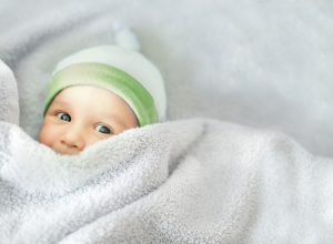 gender-neutral baby in a green hat and under covers