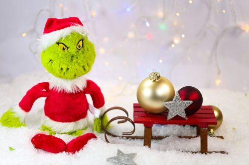 A Grinch Christmas ornament sitting next to a sleigh and ornaments.