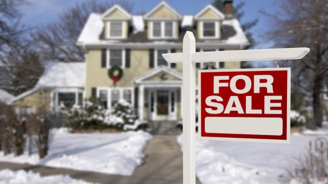 A "for sale" sign in front of a house covered in snow
