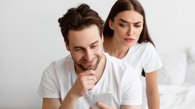 A suspicious-looking woman looking over her male partner's shoulder at his text messages.